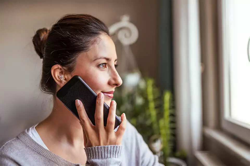 Woman with hearing aid holding phone up to ear looking out the window