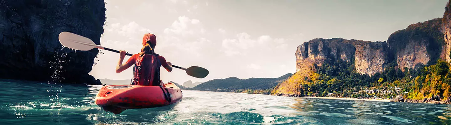 Woman kayaking in blue water next to tall cliffs