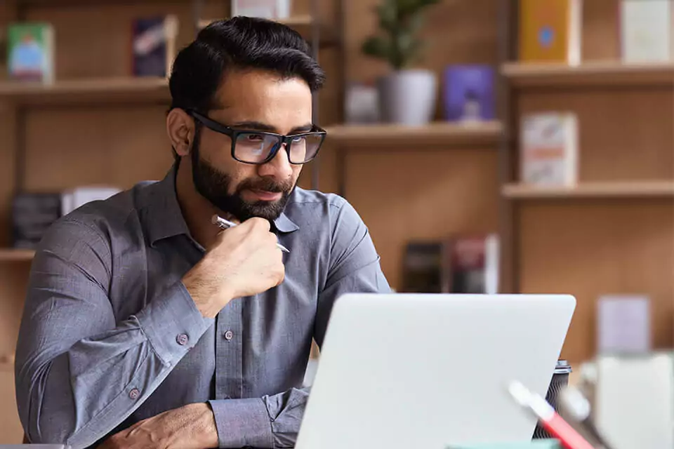 Man with glasses looking at a laptop at a table