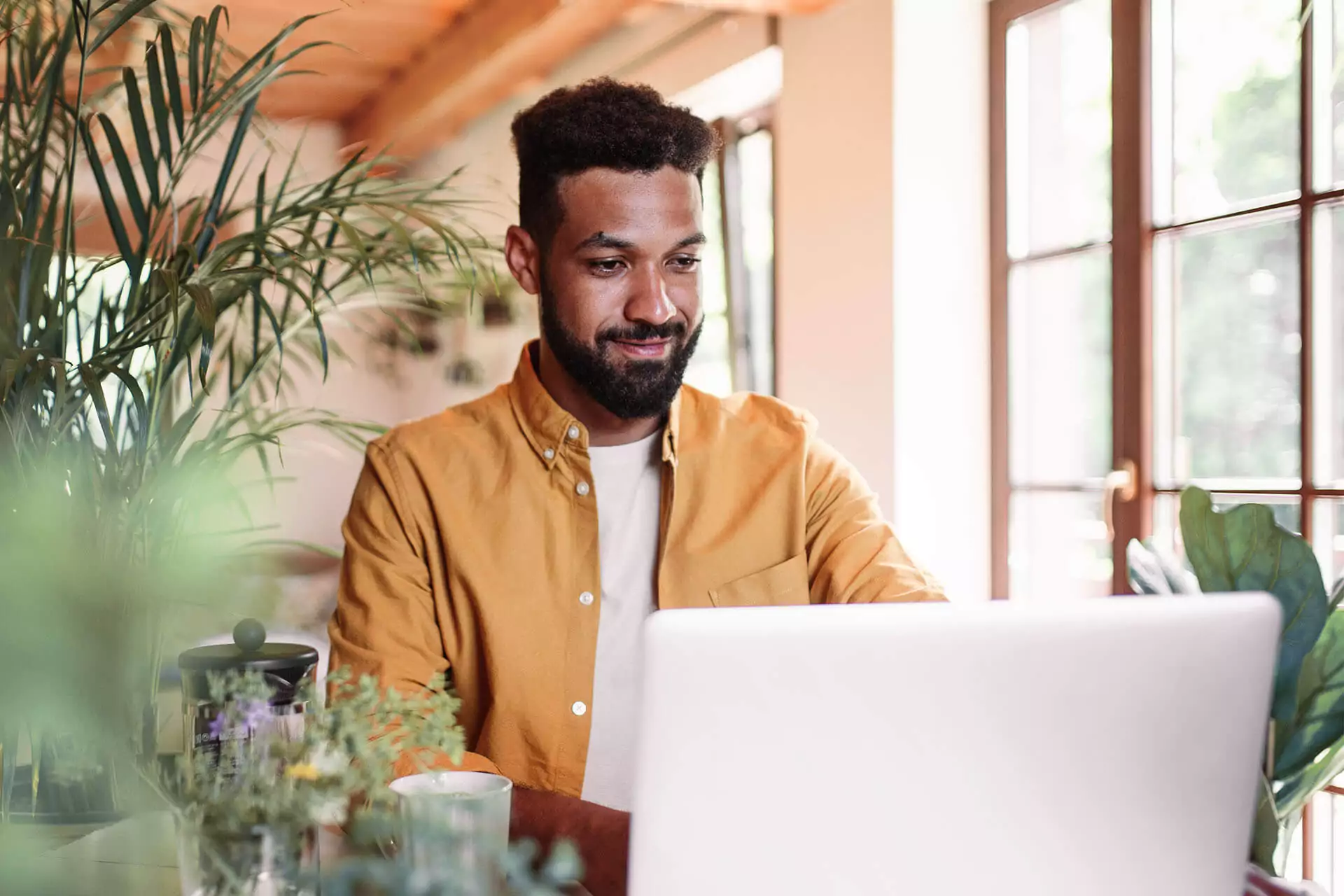 Man in yellow shirt working on a laptop in a coffee shop