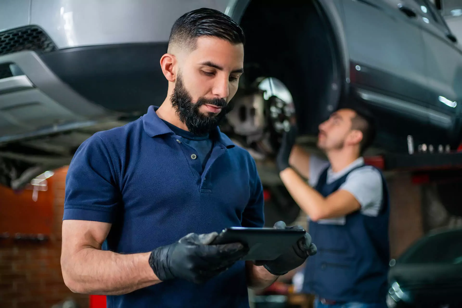 Man with black latex gloves on looking at a tablet in an auto garage